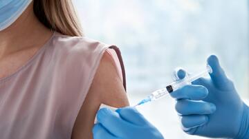 Close up view of the injection of a vaccine through a syringe into the arm of a person wearing a mask.